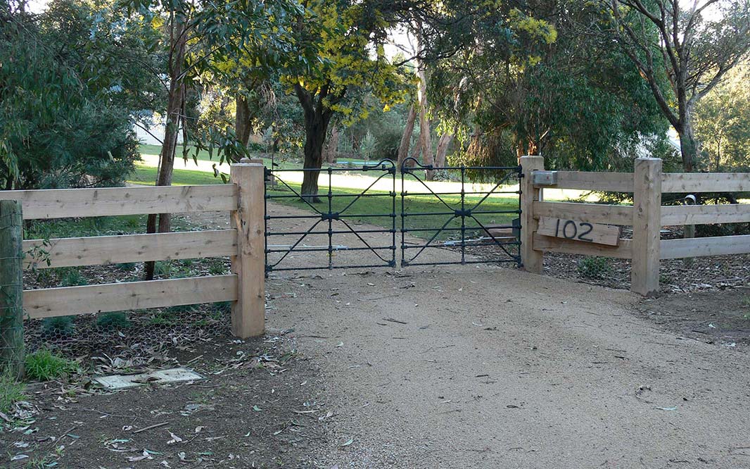 An open gate leading to the road, surrounded by post and rail fencing