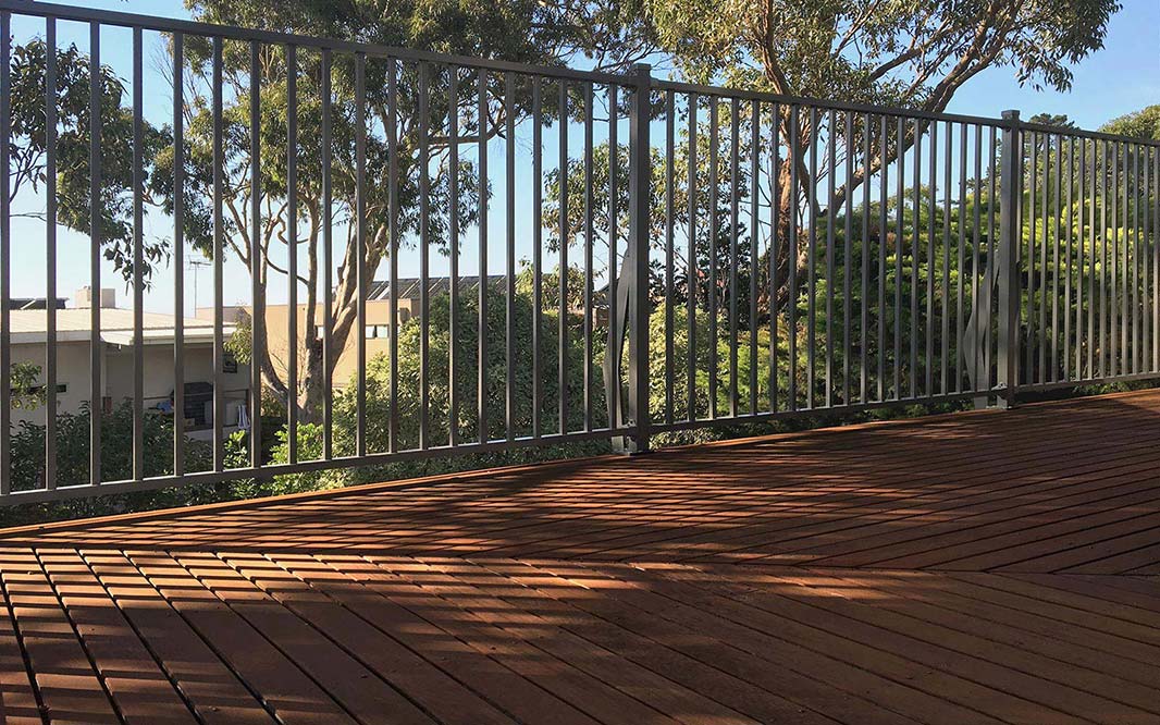 A wooden deck with an aluminium fence and trees in the background